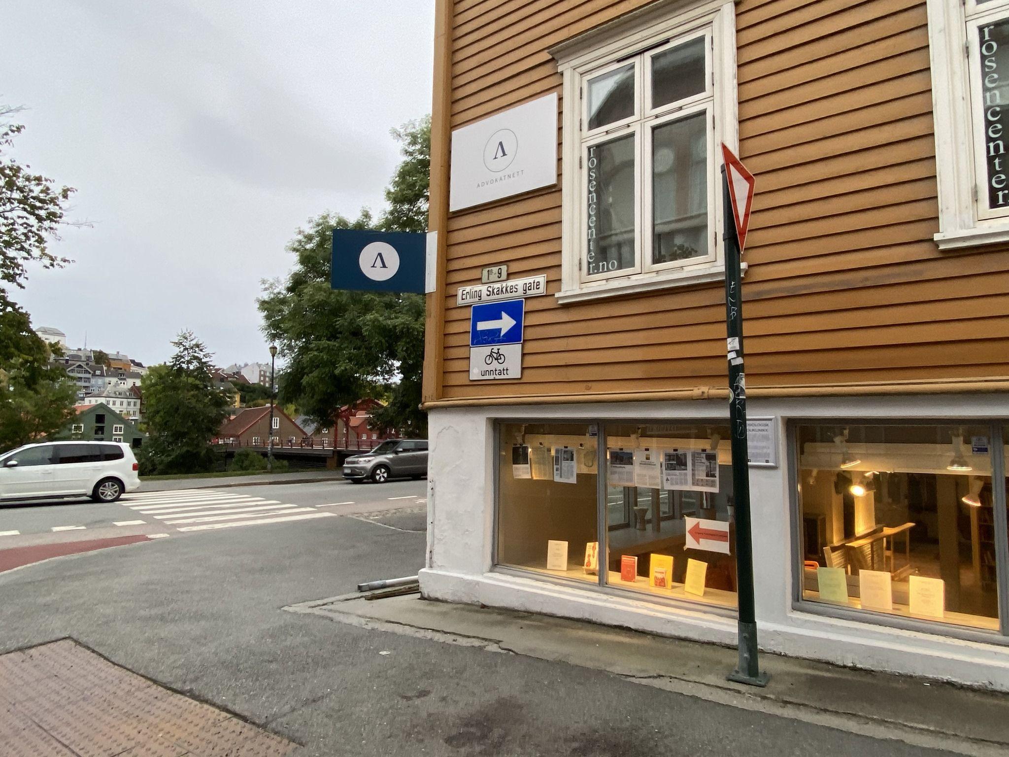 Gatehjørne med en bygning i tre, skilt som peker til venstre, og en bil som kjører forbi.