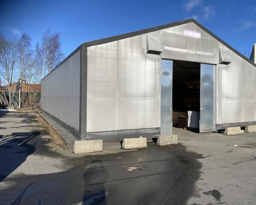 Lagerbygning med grå plastvegg og store dører, plassert på en asfaltert parkeringsplass.