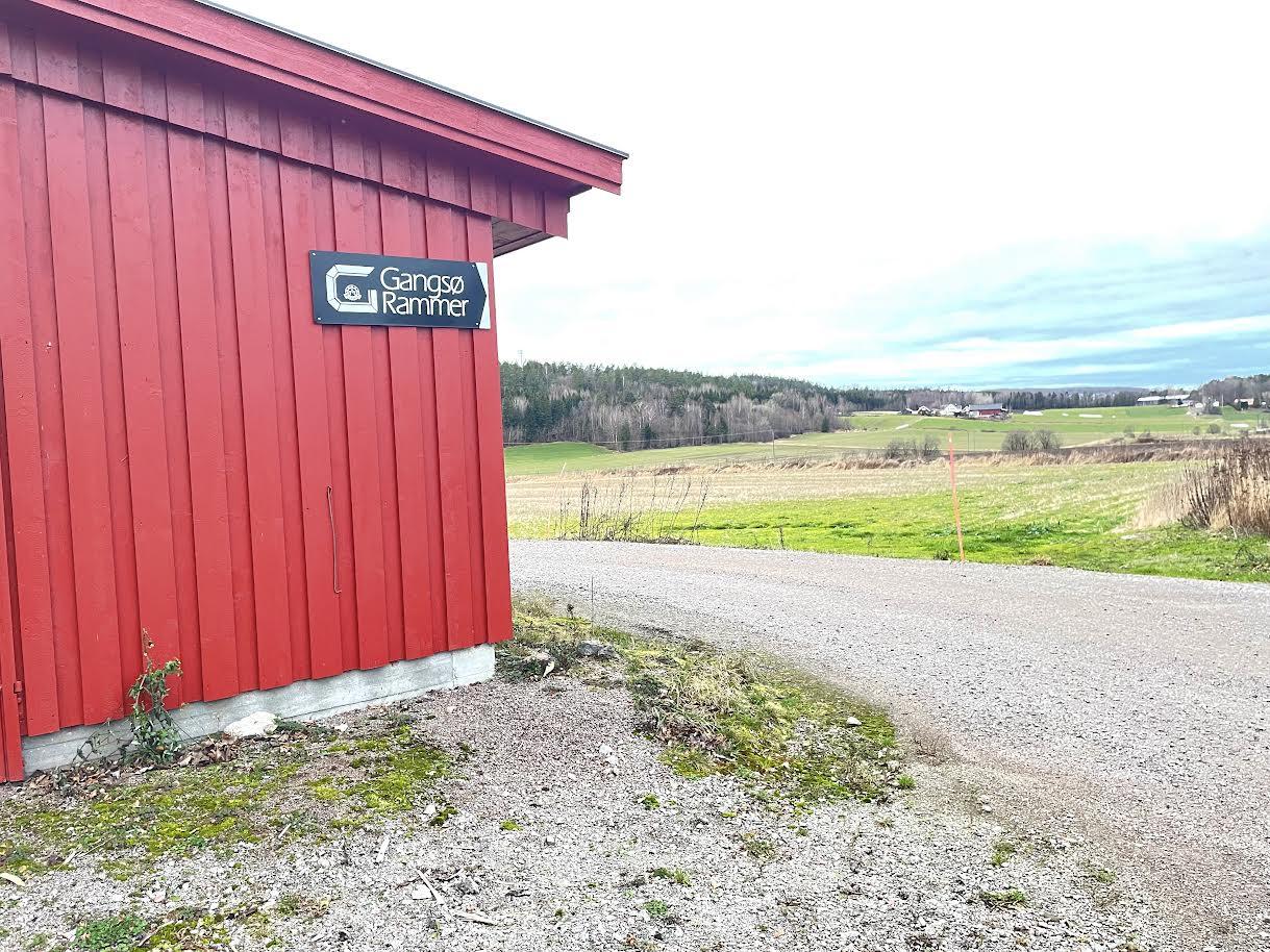 Rød bygning med skilt som viser "Gardsbryggeri" ved en grusvei og åpen landskap i bakgrunnen.