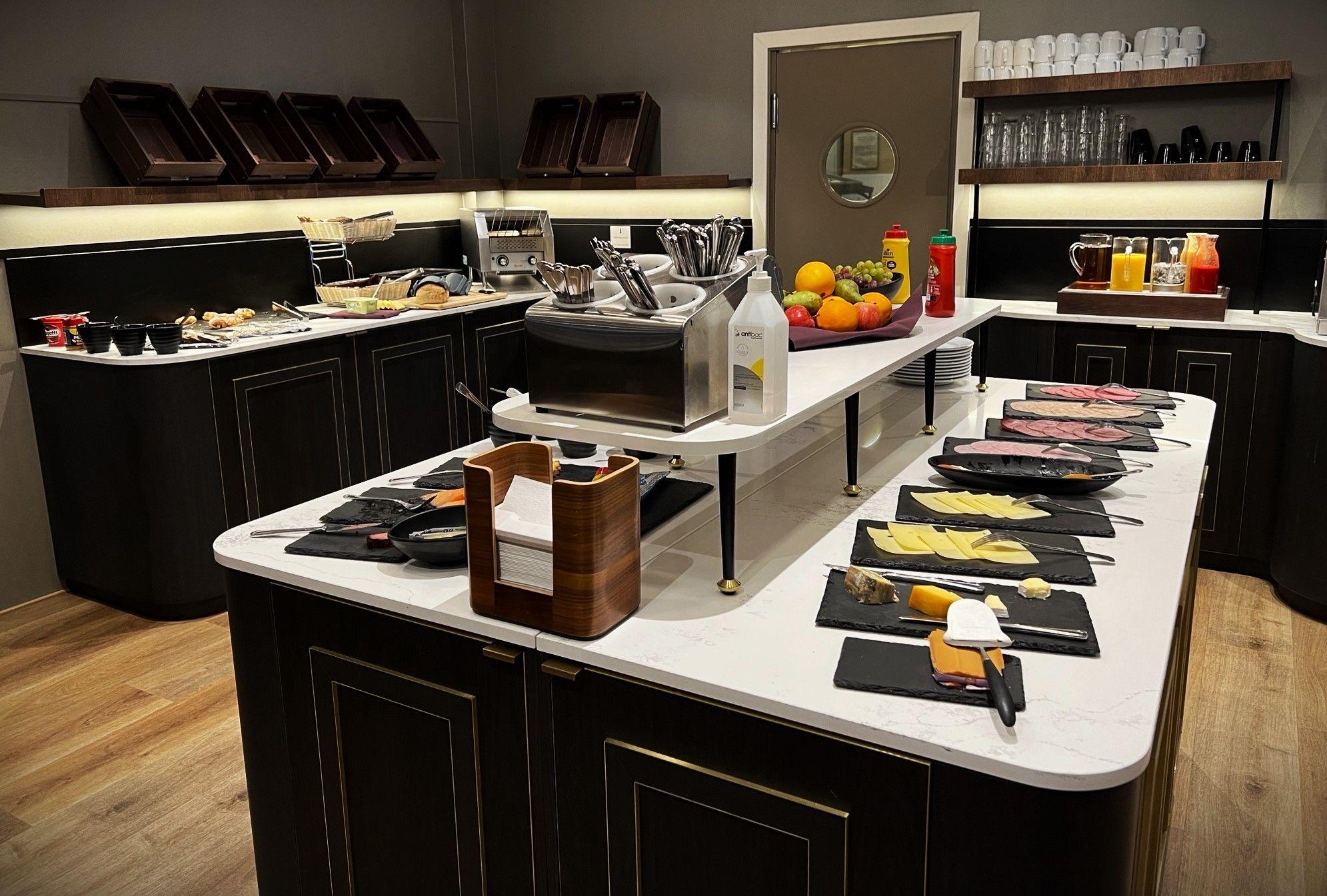 Et moderne kjøkken med et variert frokostbuffet, inkludert frukt, juice og pålegg på sorte fat.