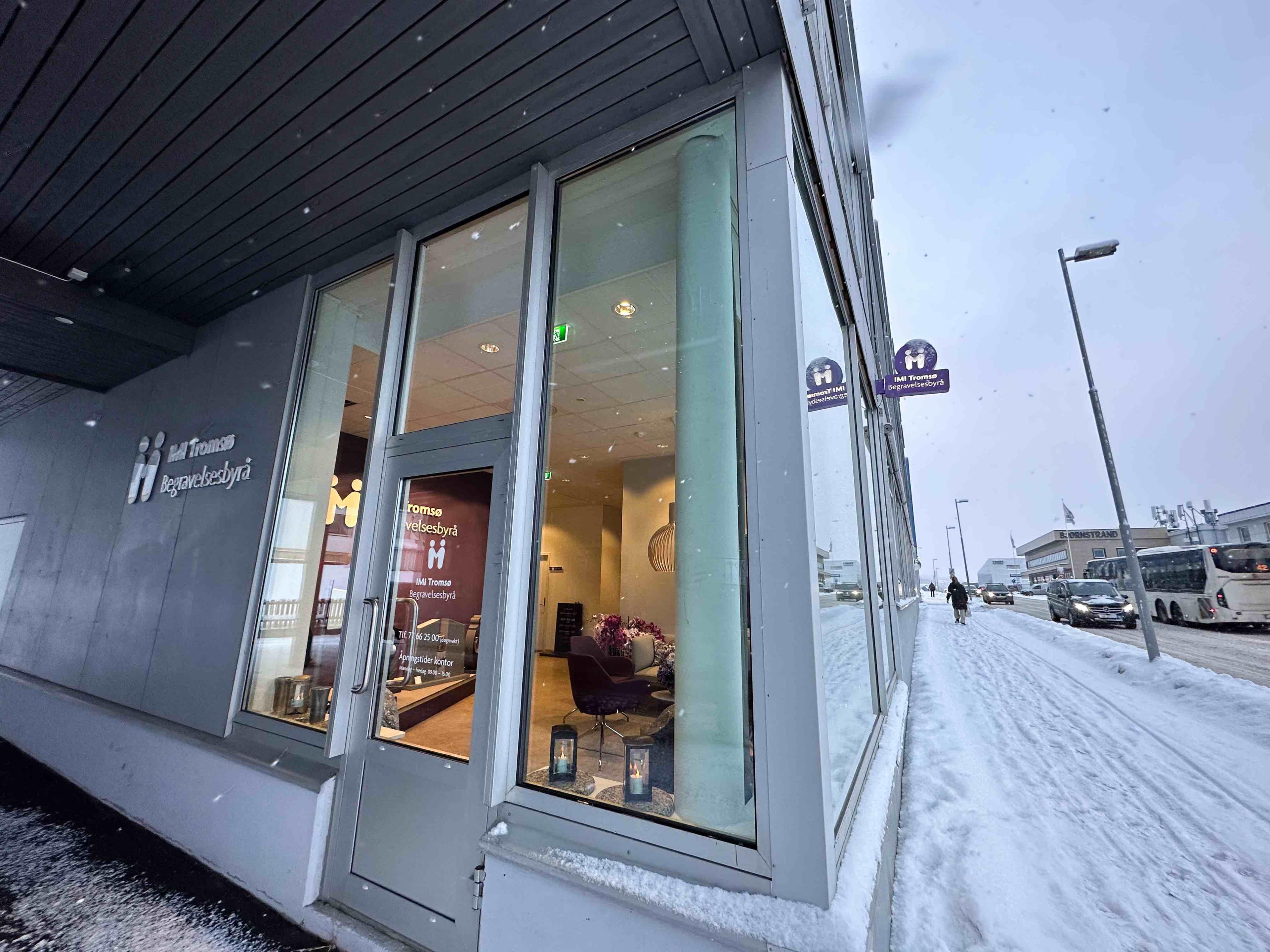 Inngangen til et moderne hotell med snø på bakken og busser parkert i nærheten.