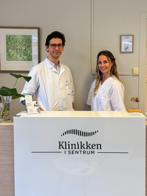 To ansatte i hvite labfrakker står ved resepsjonen i Klinikken i Sentrum.