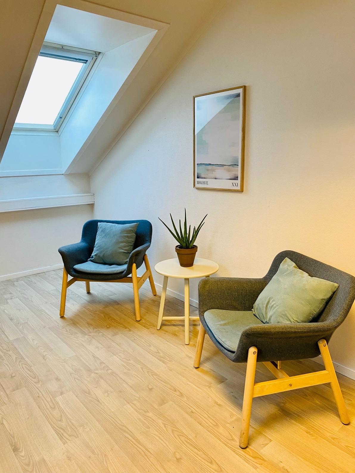 Koselig hjørne med to stoler, et lite bord og en plante under skråtaket med vindu.