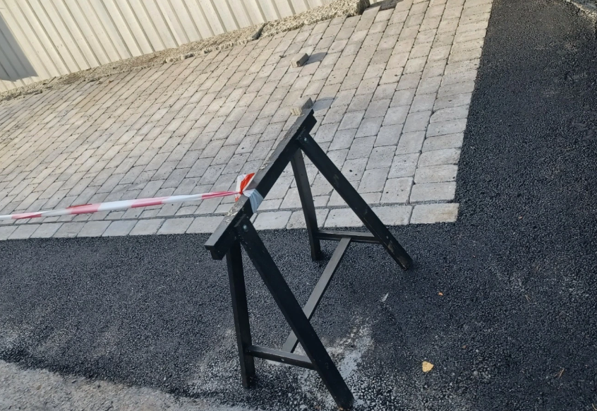 Sperrebånd og svart stige står ved siden av nylagt brostein på en asfaltert overflate.