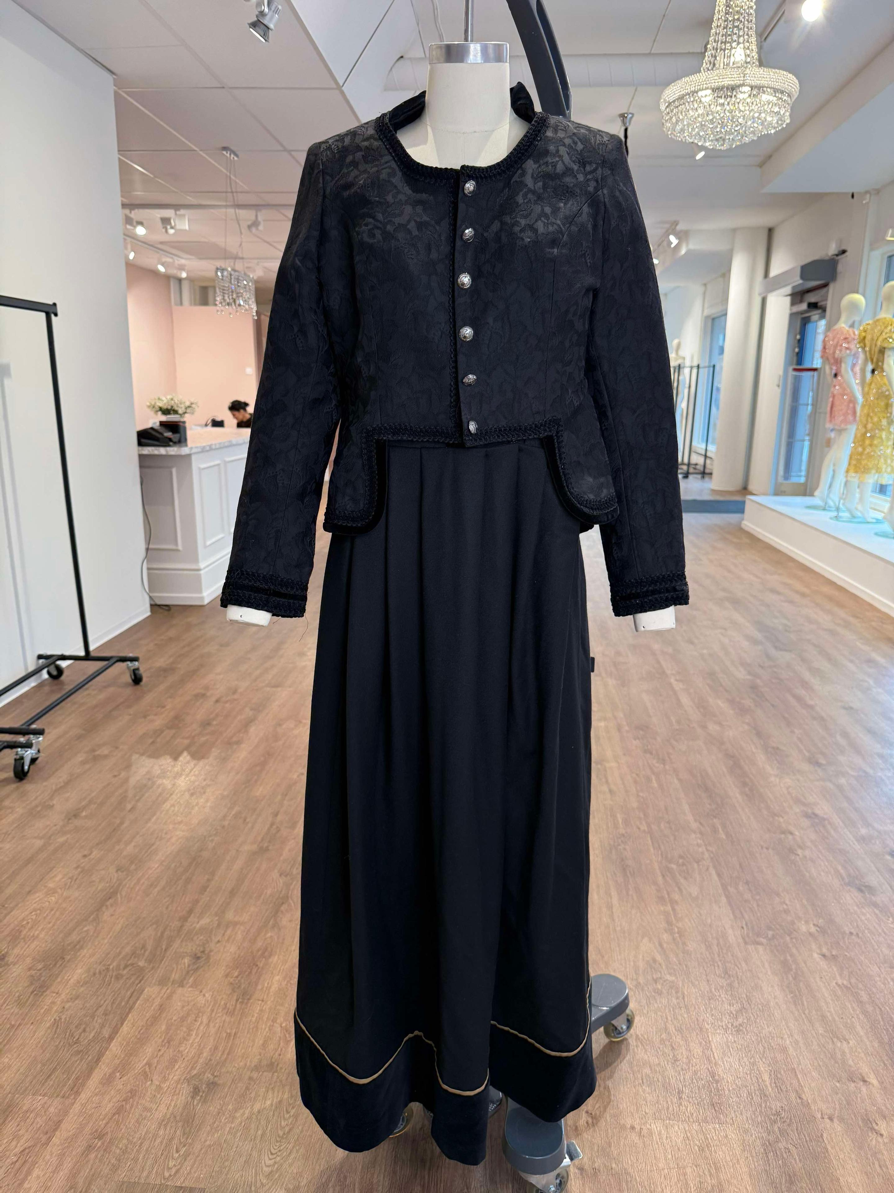 En svart kjole med jakke, utstilt på en mannequindukke i en lys butikk.