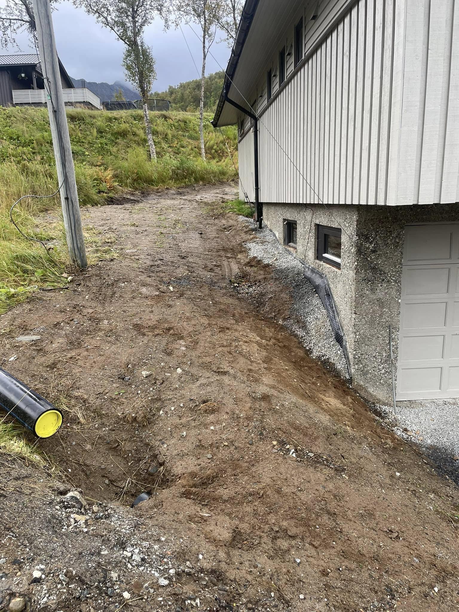 Gruslagt sti ved siden av en bygning, med rør og grønt landskap i bakgrunnen.