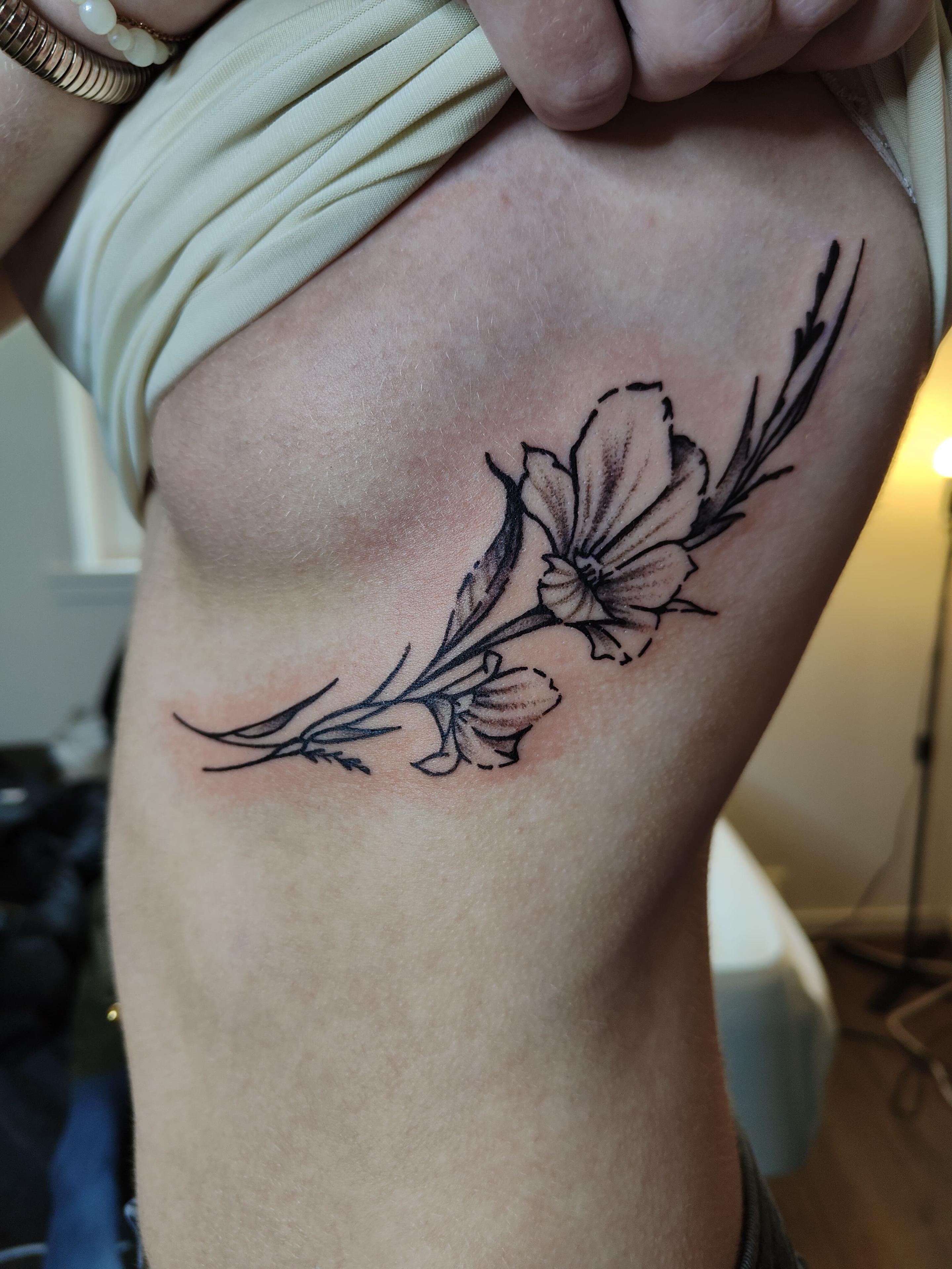 Blomster-tatovering på siden av en person, med detaljerte linjer og delikate farger.