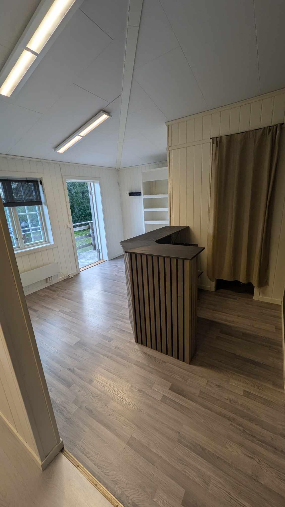Lys og romslig interiør med en trebar i front og åpne dører til hagen.