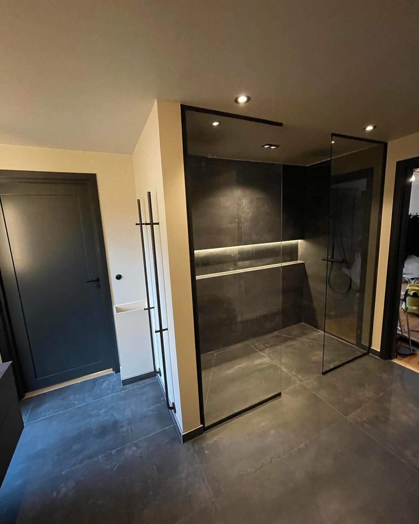 Moderne baderom med dusjhjørne i glass, mørke fliser og stilige detaljer. Døren til venstre og belysning i taket.