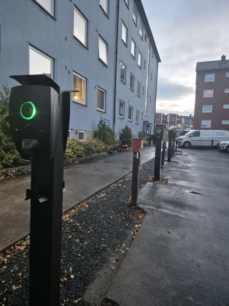 Ladepunkter for elbiler i en parkeringsplass ved en bygning, med grønne lys som indikerer tilgjengelighet.