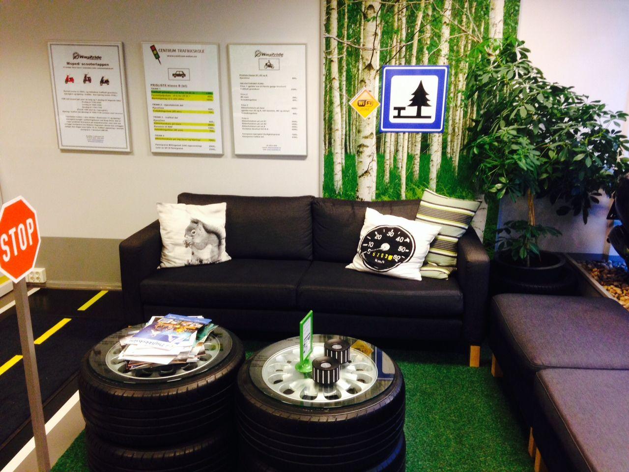 En koselig stue med en svart sofa, dekk som bord, og grønne planter på veggen med informasjonsskilt.