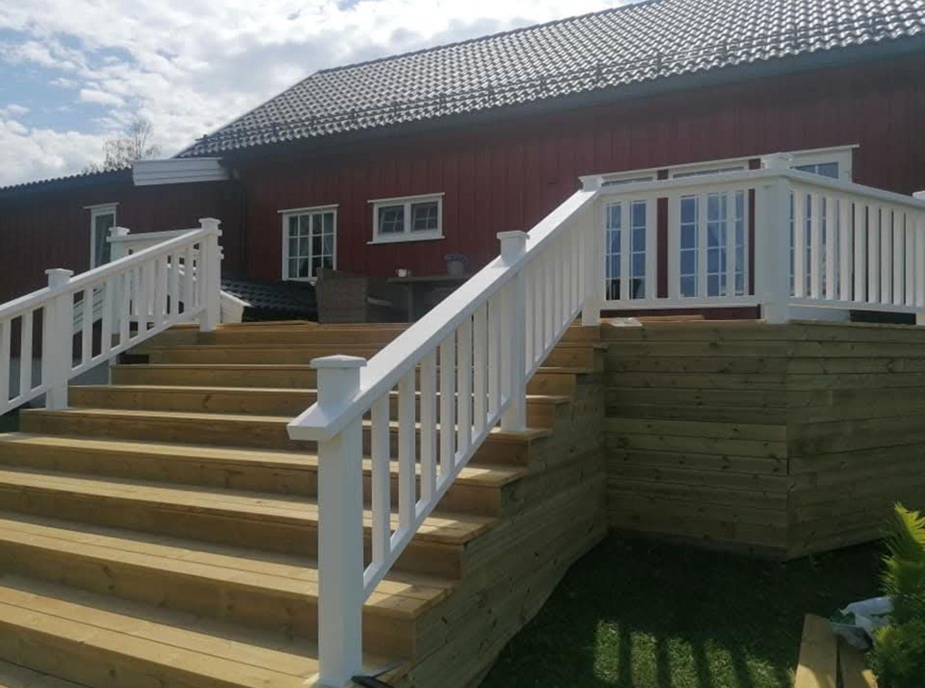En rød hytte med hvite rekkverk og tretrapper som fører opp til inngangen. Grønt gress rundt.