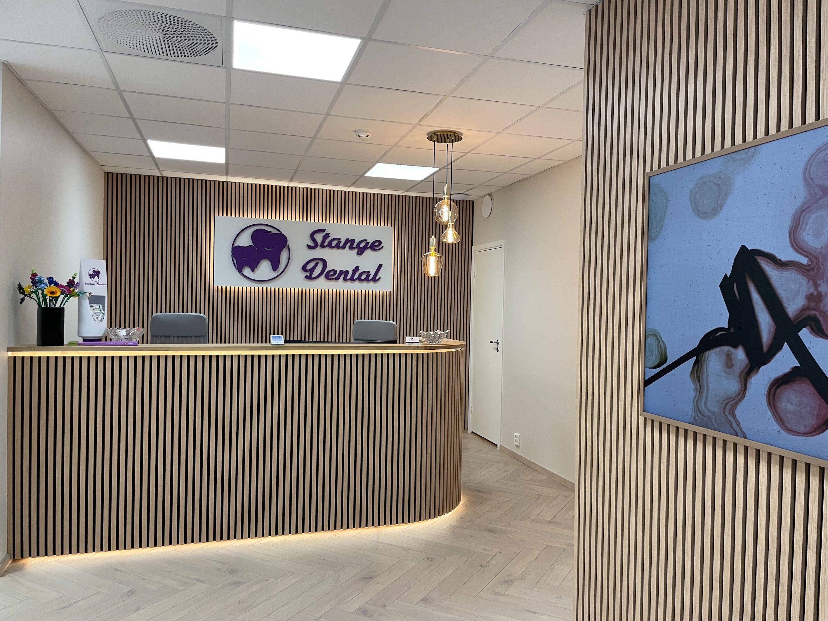 Moderne resepsjon i Stange Dental med trepanel og logo, samt kunstverk på veggen.