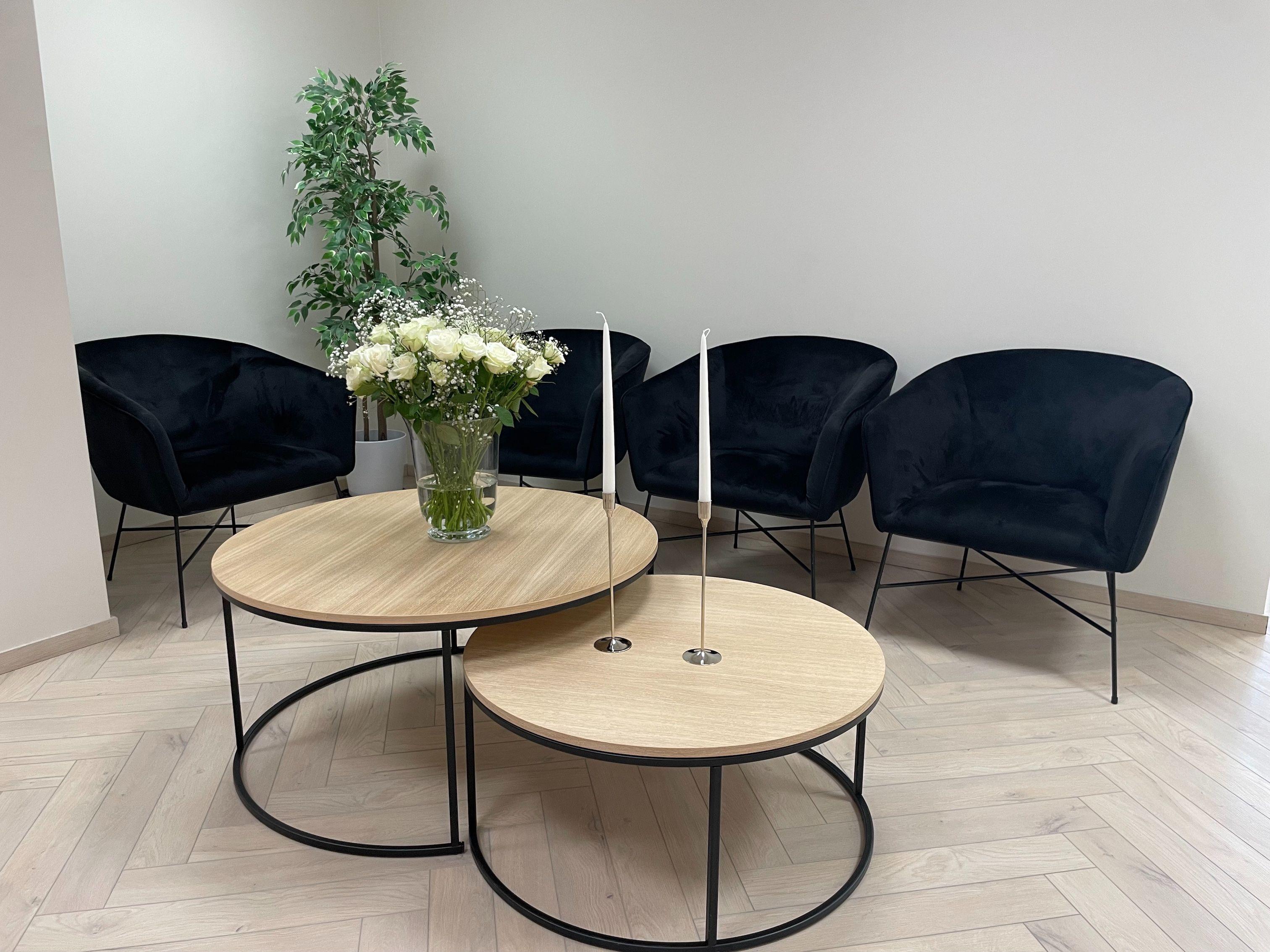 Moderne stue med svarte stoler, to runde bord i tre, og en blomsterbukett med hvite roser.