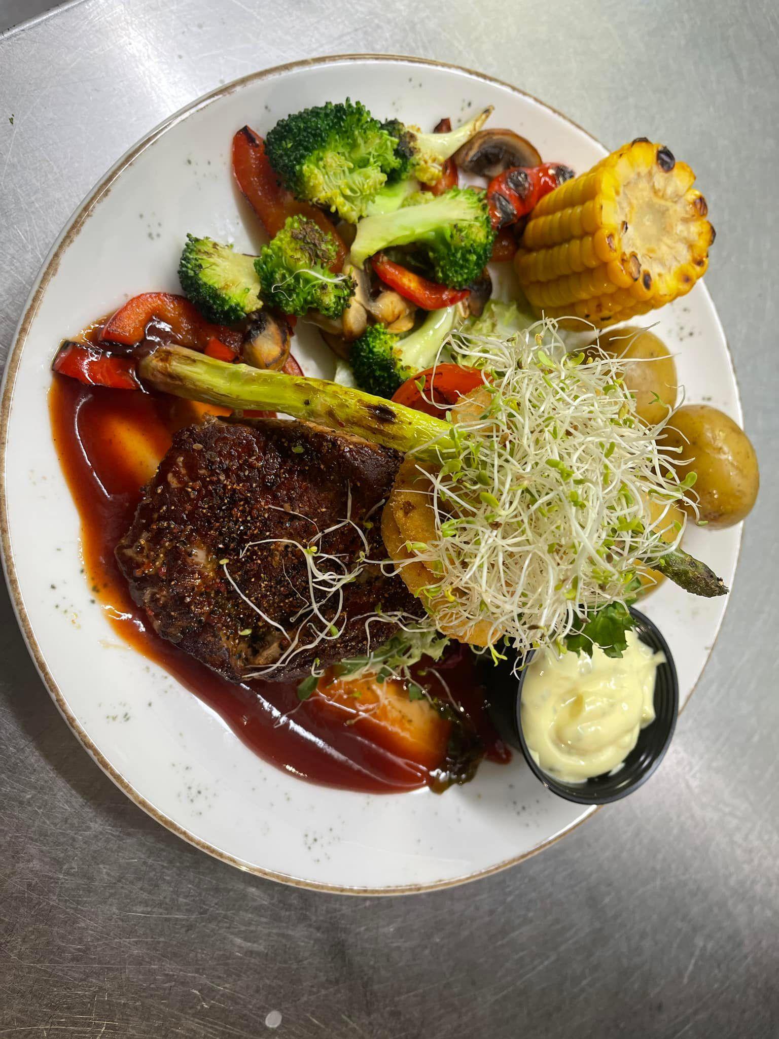 En tallerken med saftig biff, grønnsaker som brokkoli og paprika, maiskolbe og poteter, servert med saus og majones.