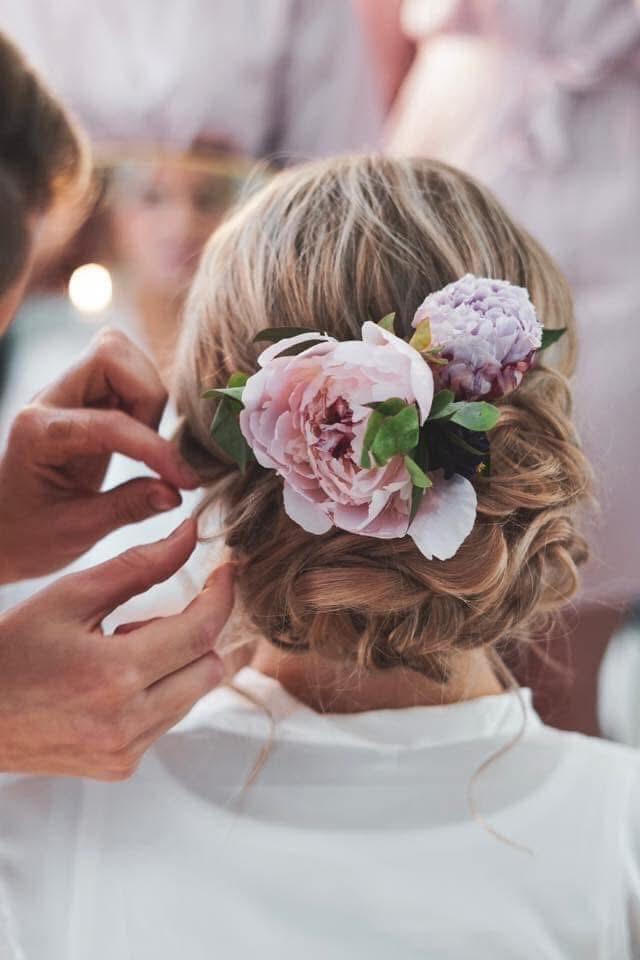 En kvinne med en elegant hårfrisyre pyntet med rosa blomster, mens noen styler håret hennes.