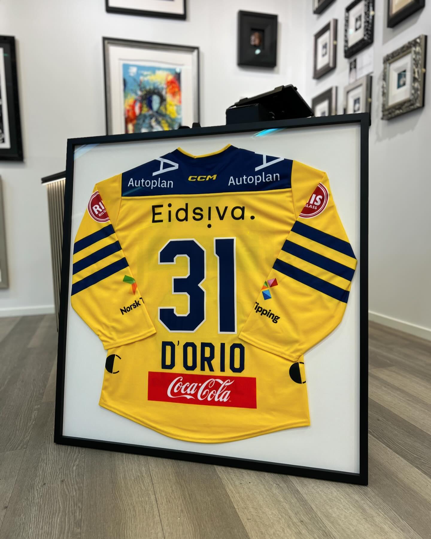 En innrammet hockeytrøye med nummer 31 og navnet D'Orio, i gult med blå detaljer og sponsorer.