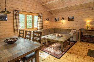 Koselig stue i en hytte med trevegger, sofa, spisebord og vinduer med gardiner.