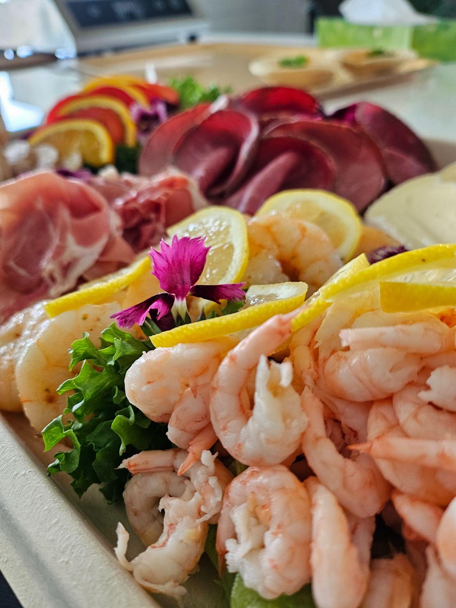 Et fargerikt fat med reker, skinke, sitron, salat og spiselige blomster, perfekt for en festlig anretning.