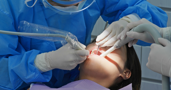 Tannlege som utfører behandling på pasient med dentalutstyr i en moderne tannklinikk.