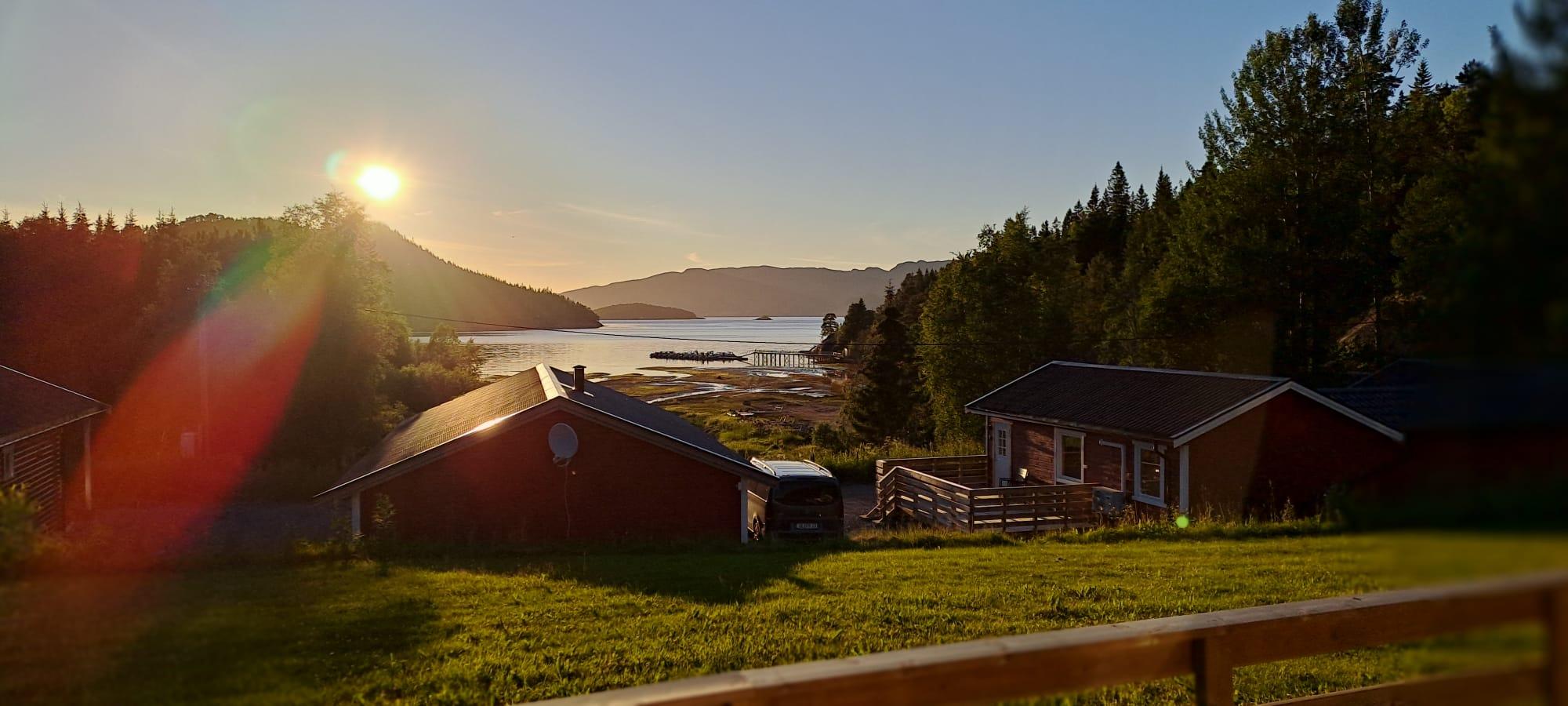 Soloppgang over en vakker fjord med hytter og grønne åser i forgrunnen.