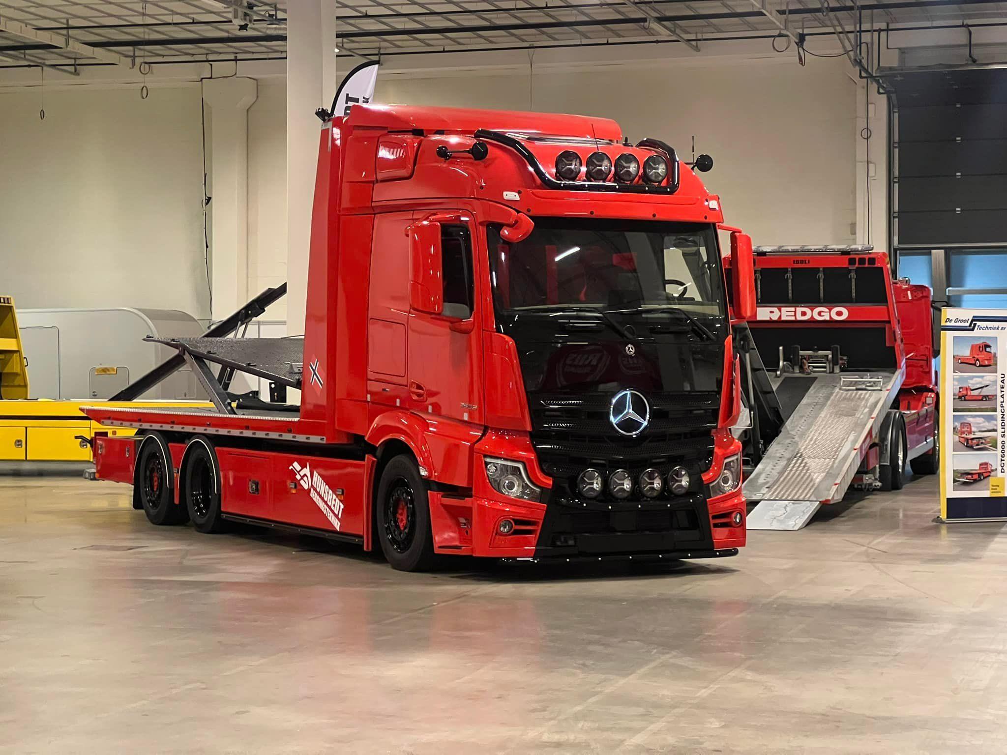 En rød lastebil fra Mercedes-Benz står i et rom med en annen lastebil i bakgrunnen.