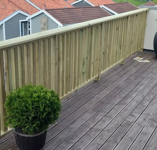 En treterrasse med en grønn plante i en potte og hus med tak i bakgrunnen.