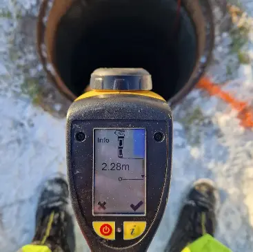 Måleinstrument som viser dybden på 2,28 meter over en brønn i snødekt terreng.