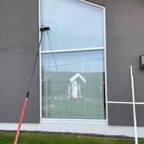 En vindusvasker med langt skaft rengjør et stort vindu på en moderne bygning.