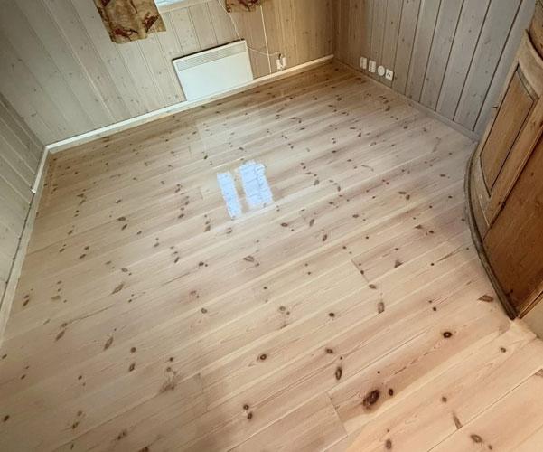Lyst tregulv i rom med vegger av trepanel og et hjørneskap.