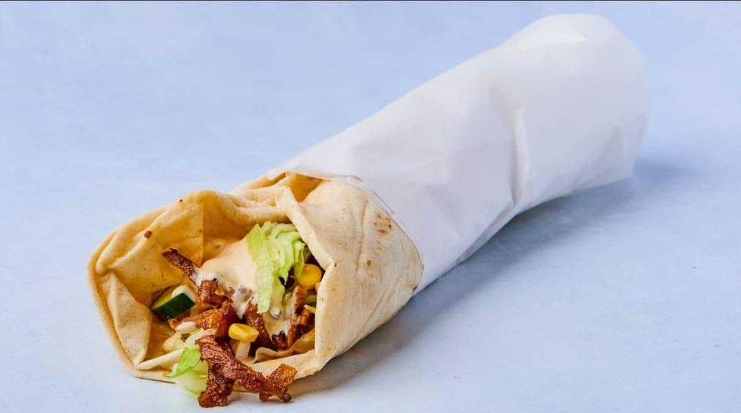 En innpakket burrito med kjøtt, salat, mais og saus, ser appetittvekkende ut på en lys bakgrunn.