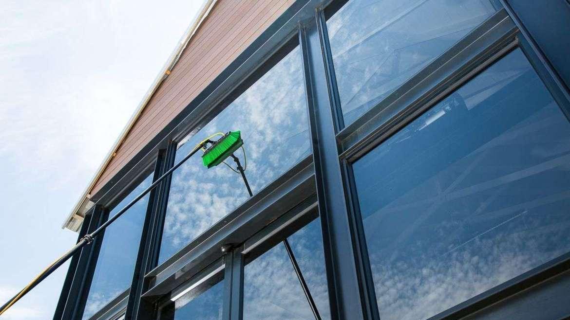 Rengjøring av vinduer på en moderne bygning med en grønn vindusvasker.
