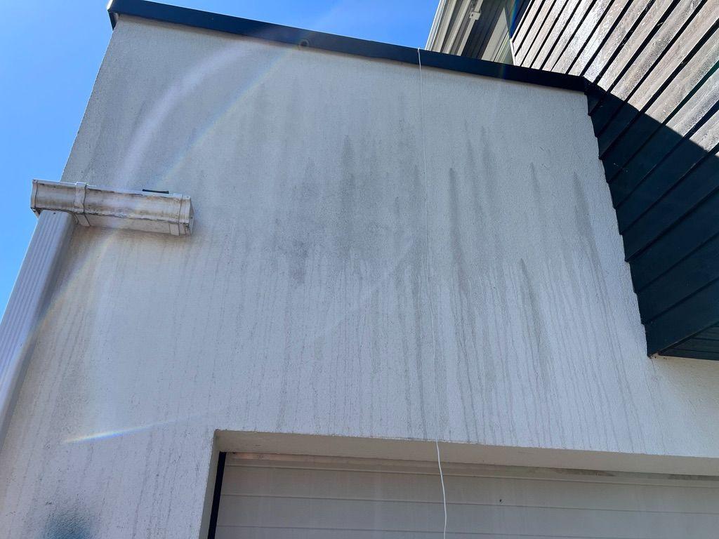 Fasade på hus med synlige flekker og skitt, under klar himmel.