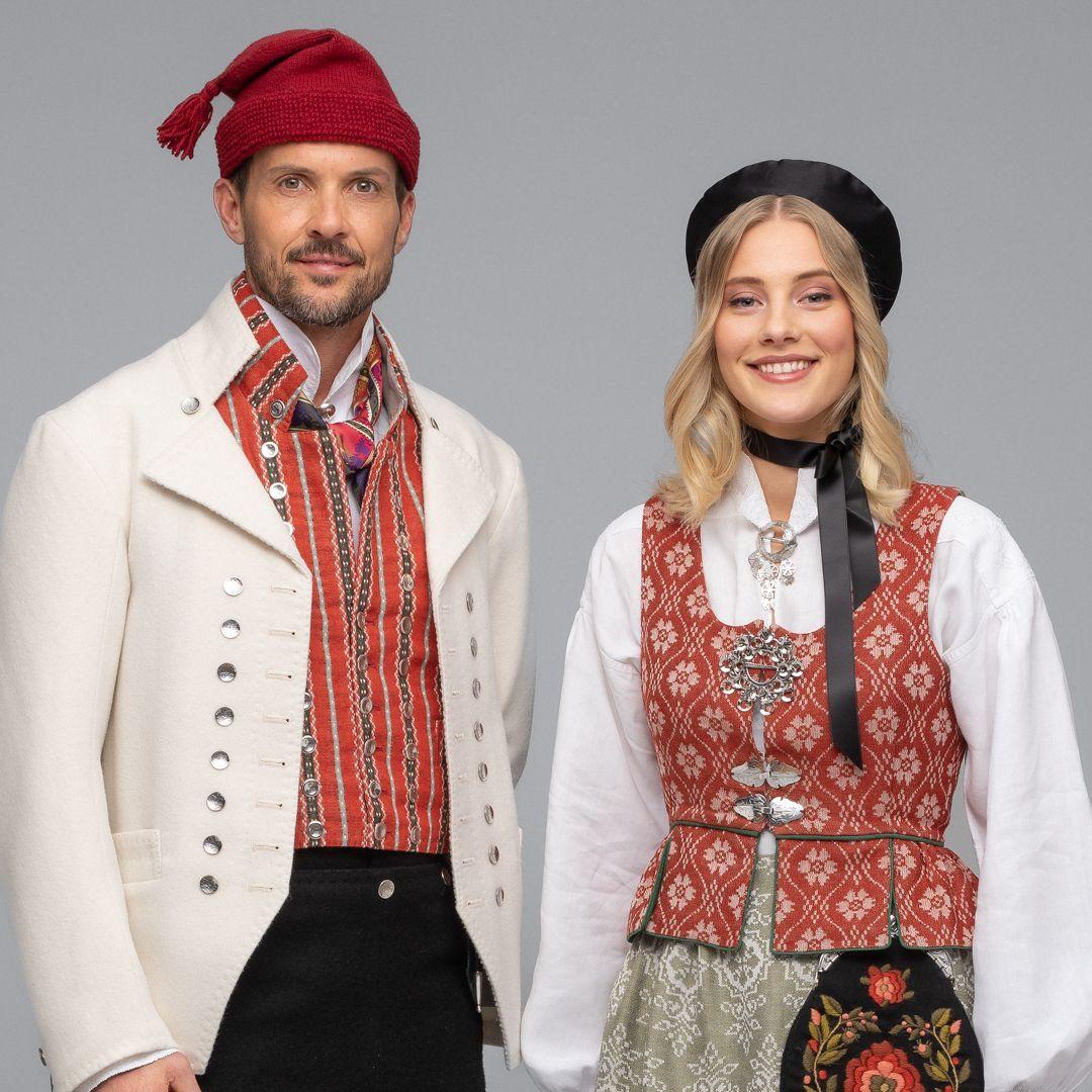 Mann og kvinne iført tradisjonelle norske bunader med detaljerte mønstre og tilbehør.