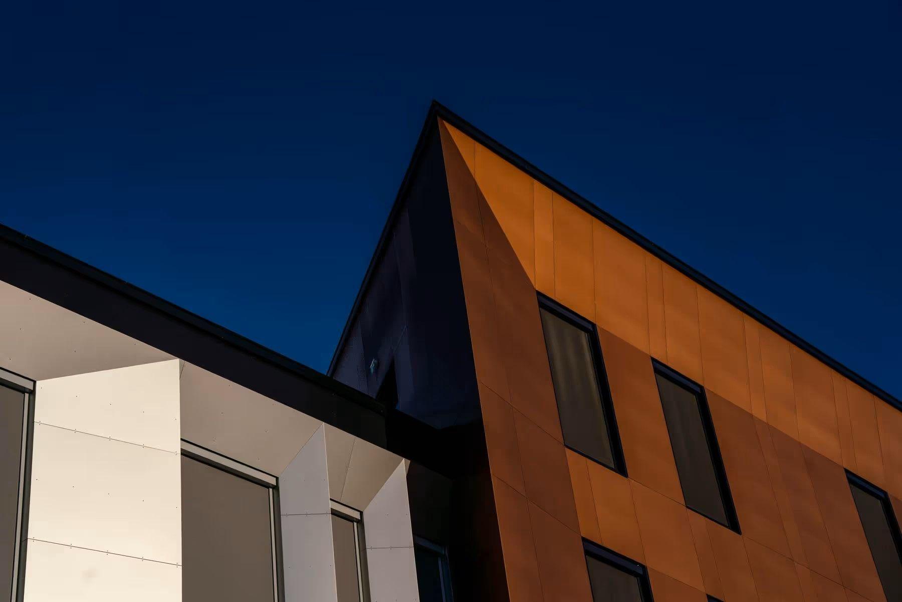 Moderne bygning med en kombinasjon av hvite og brune fasader under en klar blå himmel.