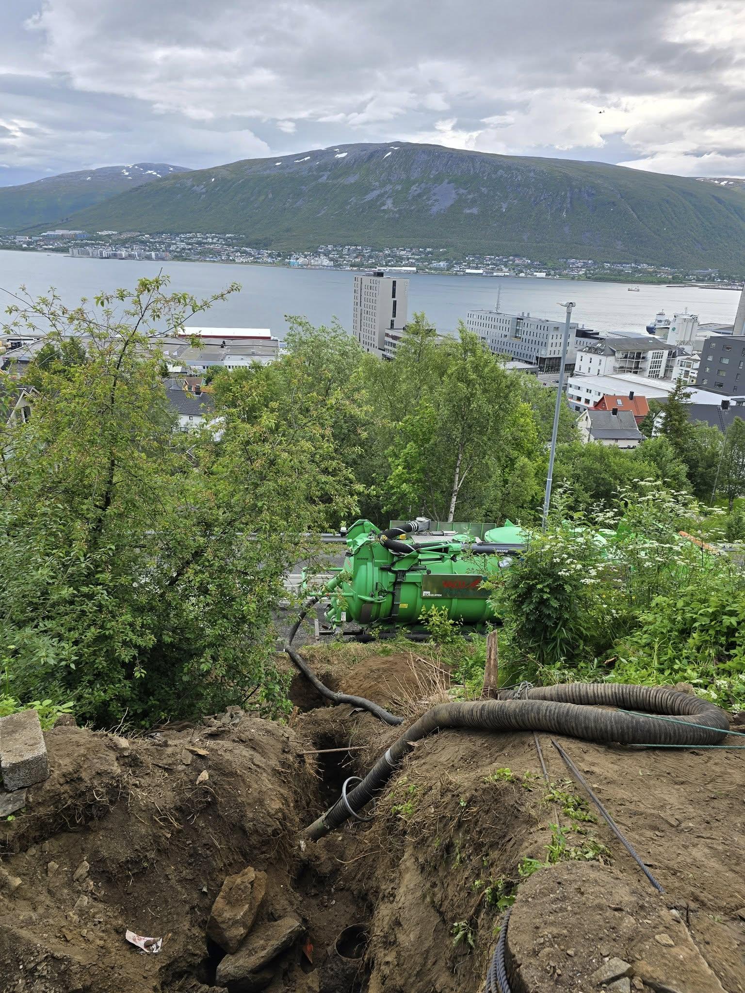 Utsikt over en grønn maskin i en grøft, med fjorden og fjellene i bakgrunnen.
