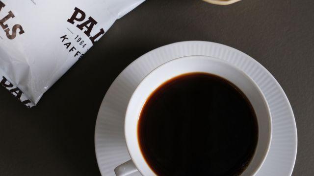 Kopp med svart kaffe på en grå overflate, med en kaffepose ved siden av.