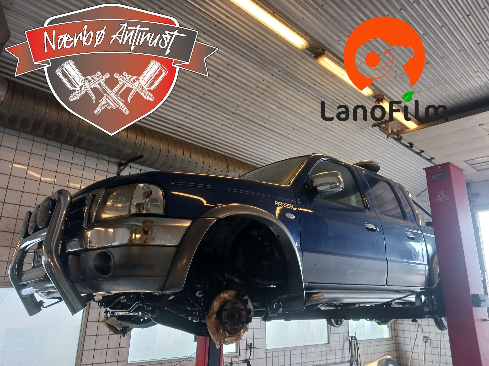 Blå SUV hevet på en bilheis i et verksted med logoer for Nermo Autolust og LanoFilm.