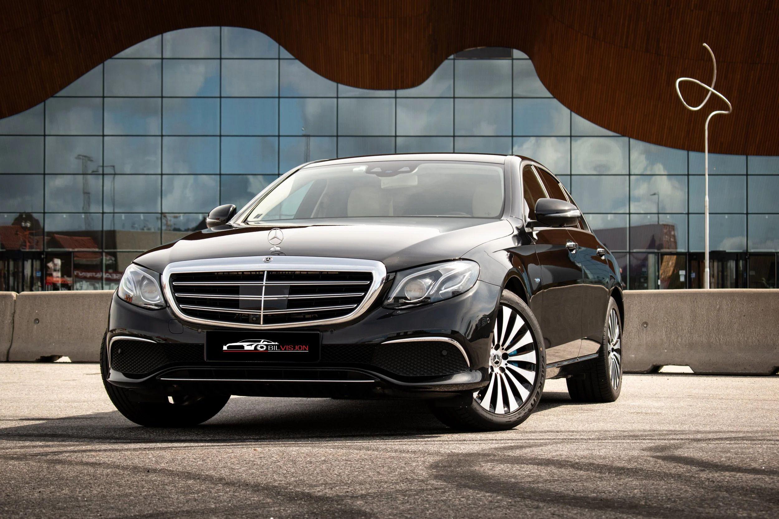 En svart Mercedes-Benz E-klasse sedan parkert foran en moderne bygning med glassfasade.