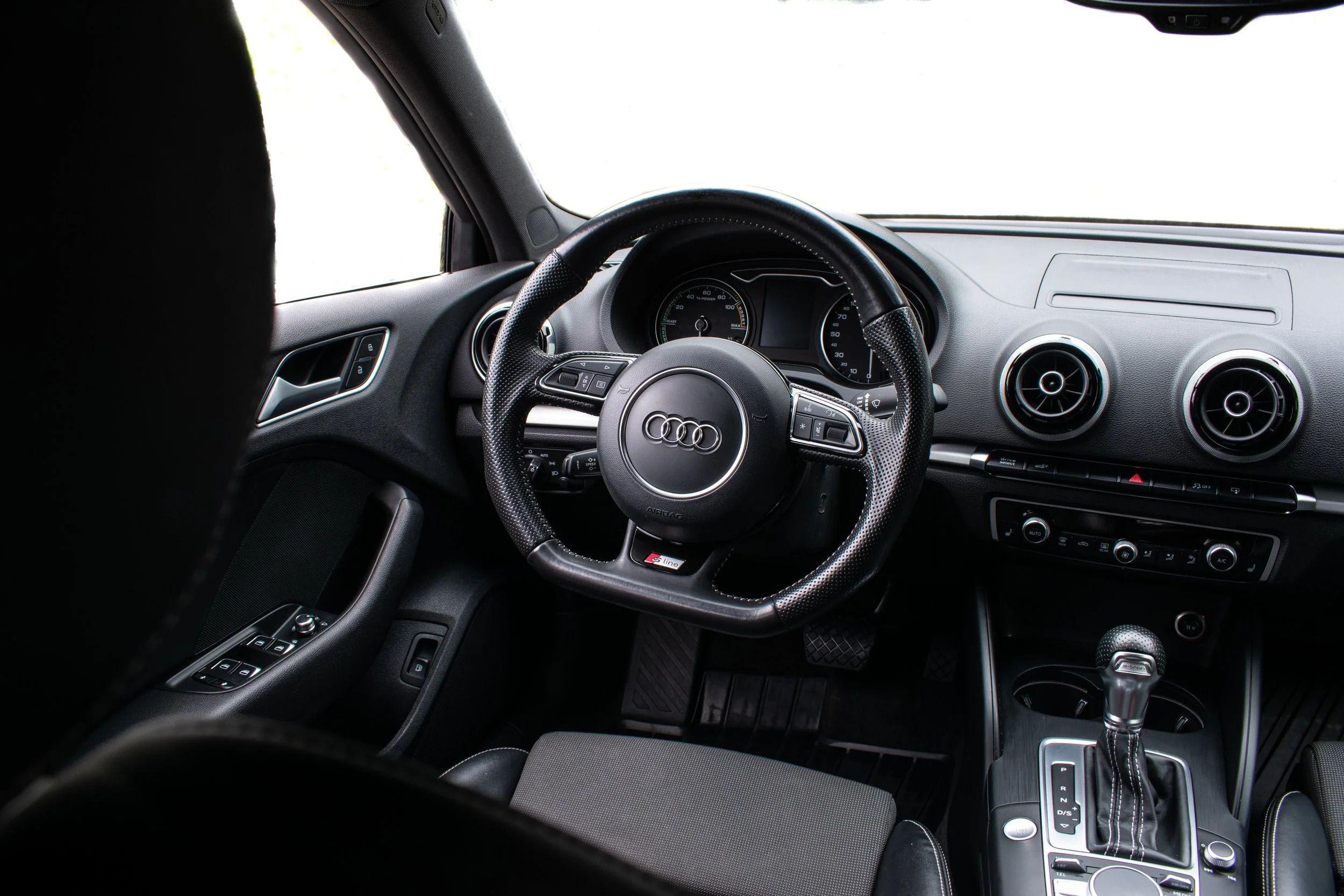 Interiør av en Audi med ratt, instrumentpanel og girspak, fokus på detaljer og moderne design.