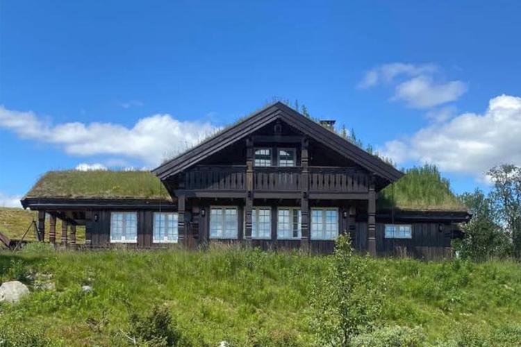 En vakker hytte med torvtak, beliggende i grønt landskap under en blå himmel.