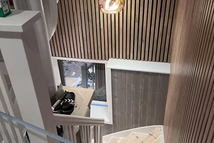 Trappen med trepanel og moderne belysning, sett fra oven, med vindu og sko på trappen.