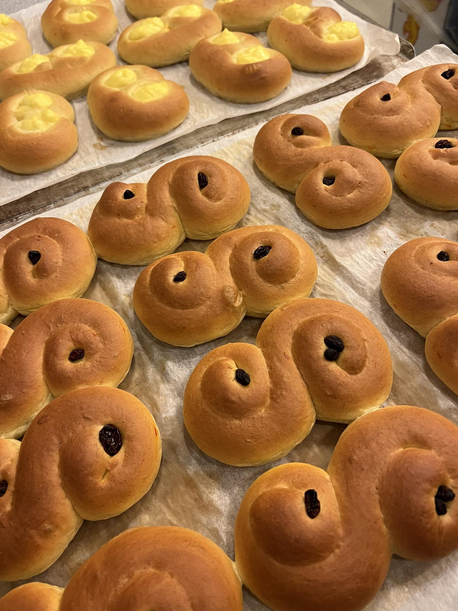Nystekte lussekatter med rosiner, plassert på bakepapir, klare til å bli servert.