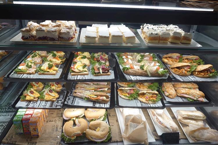 Et utvalg av bakverk og smørbrød i en delikatessebutikk, inkludert kaker, salater og brød.