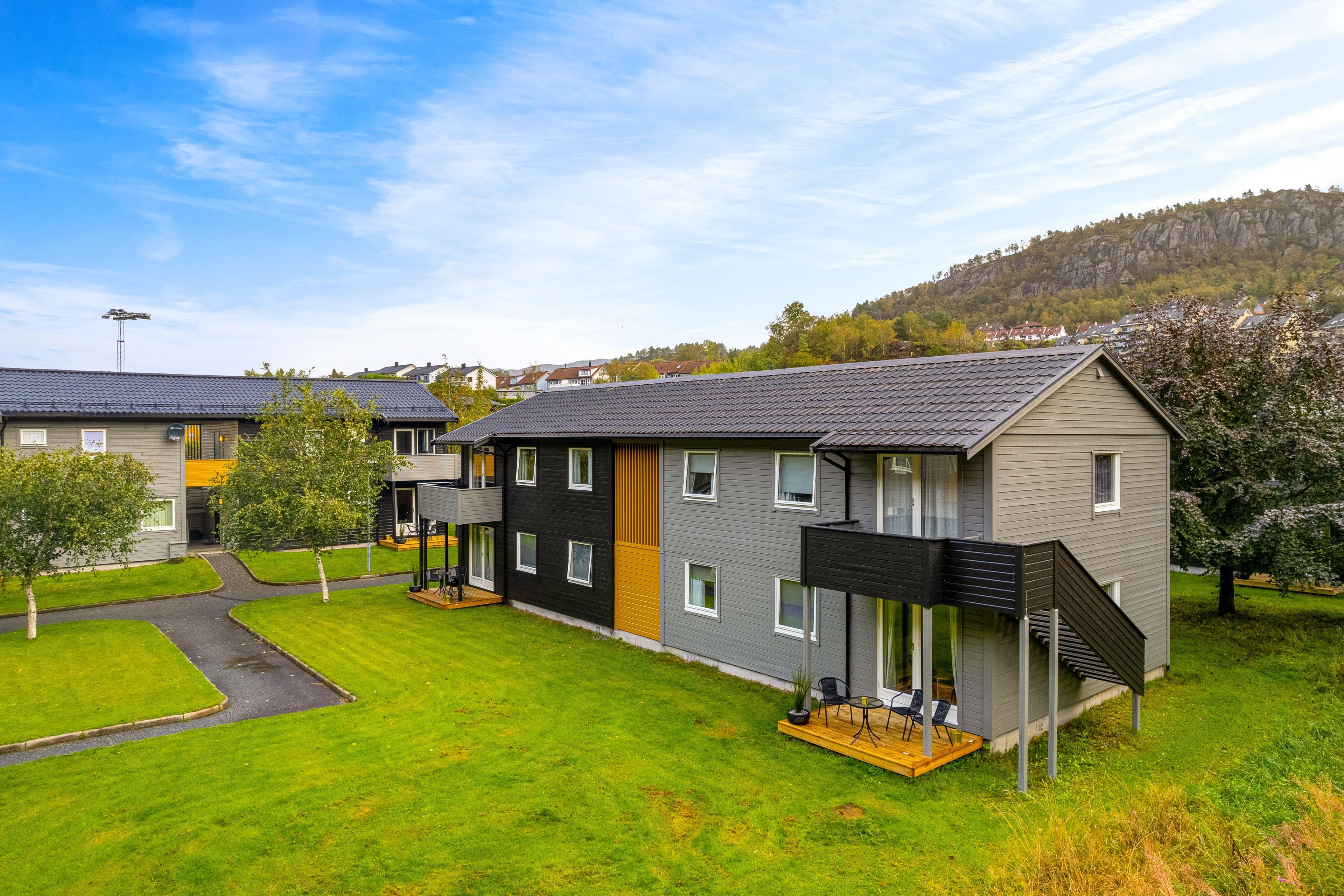 Moderne leilighetsbygg med grønt gress og trær, beliggende i naturskjønne omgivelser.