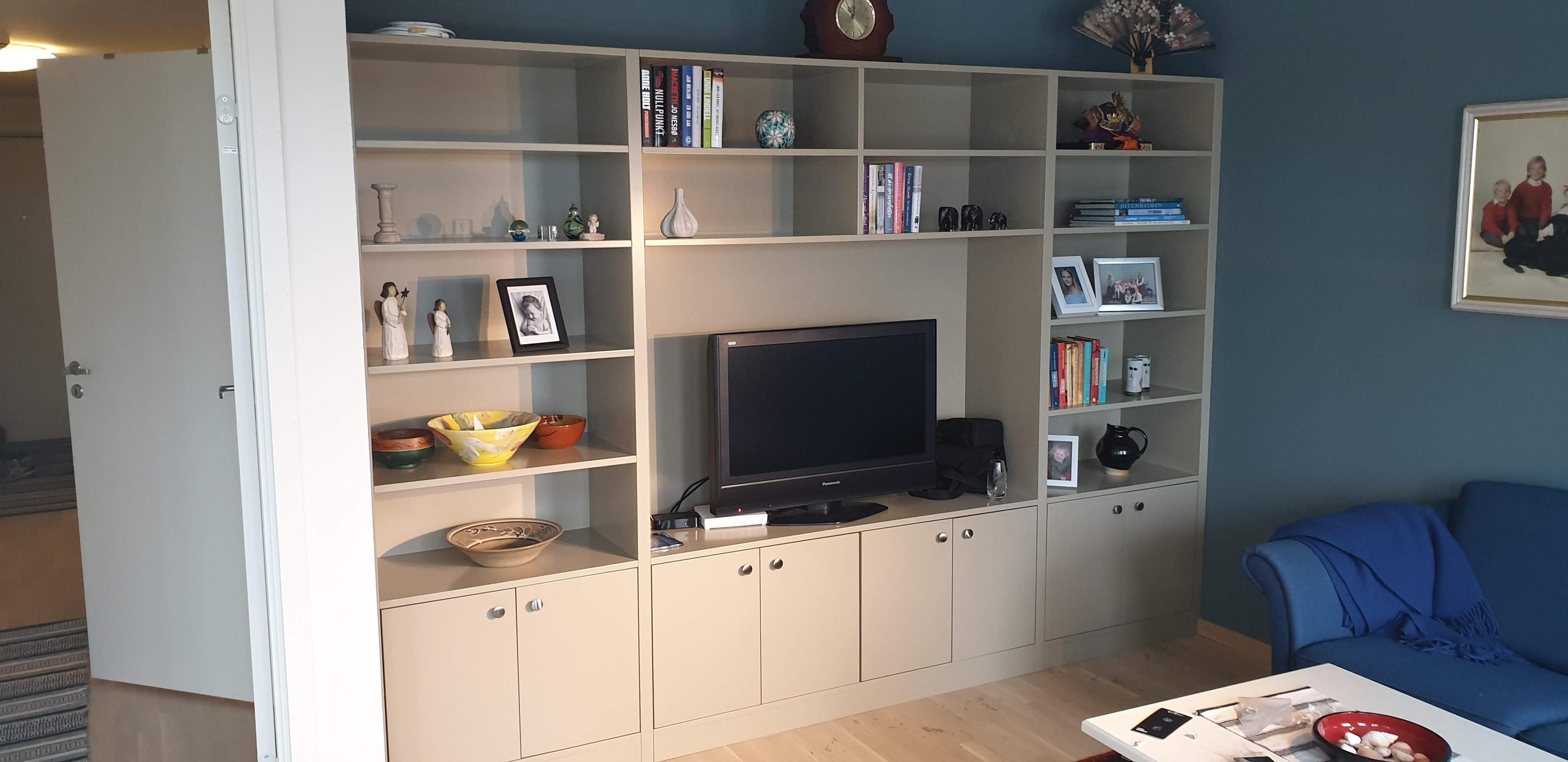 Stue med en TV, bokhyller og en blå sofa, samt dekorative gjenstander og bilder på hyllene.