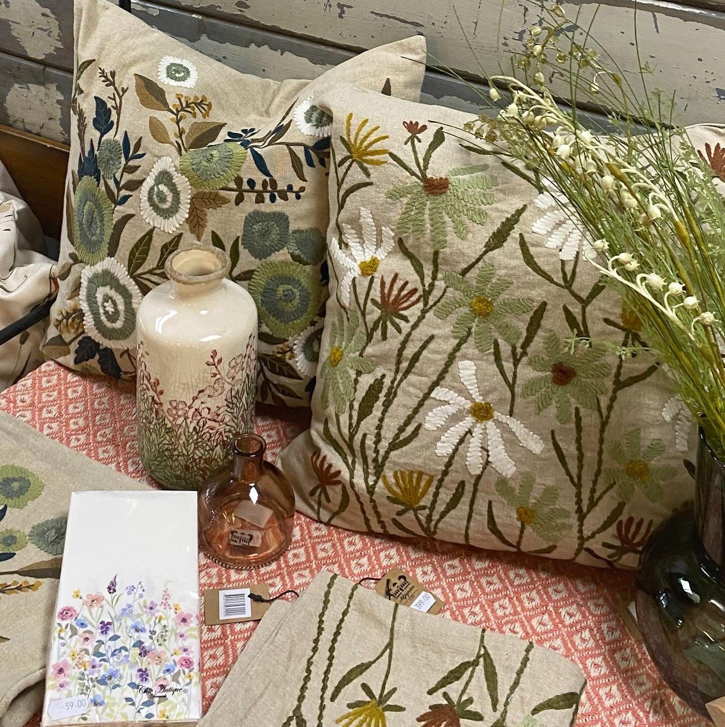 Dekorative puter med blomsterbroderi, en vase, og en maleri på et bord med tekstil i pastellfarger.
