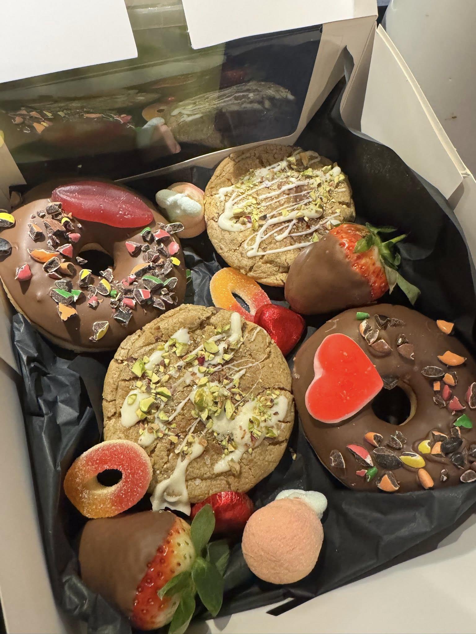 En boks med deilige kaker, donuts, sjokoladebelagte jordbær og fargerike godteri.