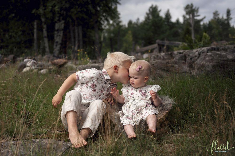 To barn som sitter på en stein i naturen, det ene barnet kysser det andre på pannen.