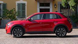Rød SUV med svarte felger parkert foran en bygning med grønne vinduer og planter.